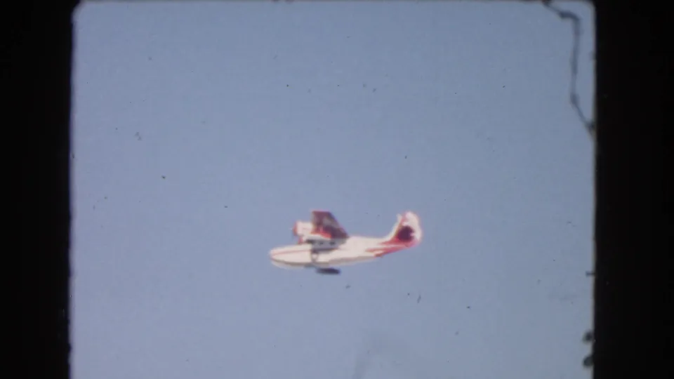 A small red-and-white seaplane flies across the blue sky in the 1966 Los Angeles home-movie clip.