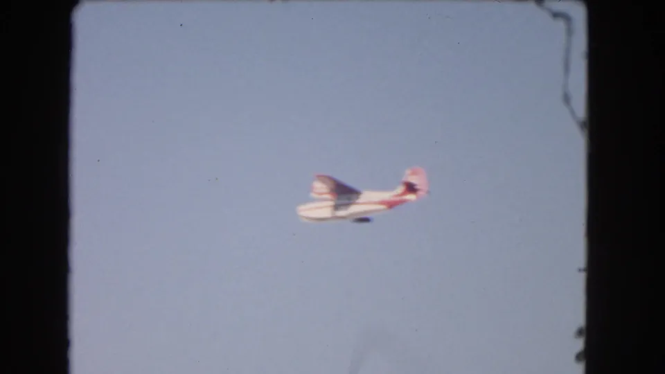 The small red-and-white seaplane remains centered low in the frame against pale blue sky in the 1966 Los Angeles footage.
