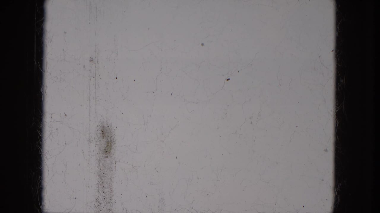 1966 8mm frame sample from Milwaukee metadata with pale exposure, black frame edges, a vertical stain, dust, scratches, and film grain.