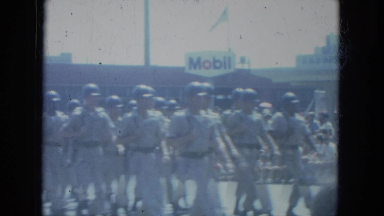 Uniformed soldiers march in formation on a Milwaukee street, with a Mobil gas station sign visible behind them.