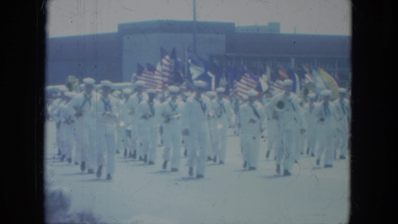 Sailors in white uniforms march with American flags during a civic parade.