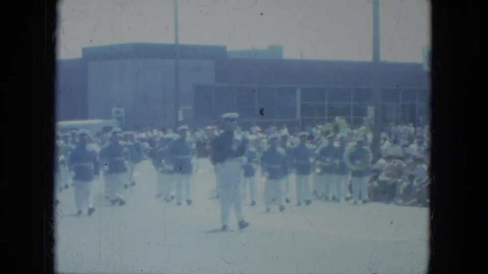 1966 Milwaukee parade frame showing a marching band and seated spectators along the sunlit street.