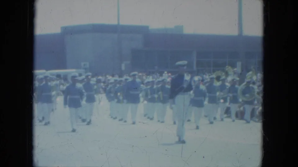 Milwaukee 1966 home-movie frame with a uniformed parade leader, band members, and spectators in the background.