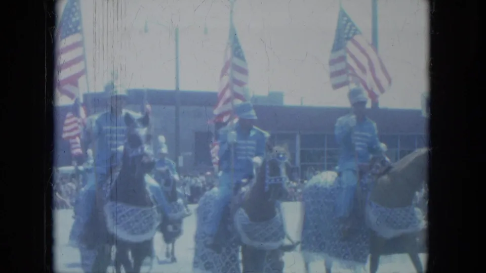 Soft 8mm frame from a 1966 Milwaukee parade with mounted riders, decorated horses, flags, and spectators in the background.