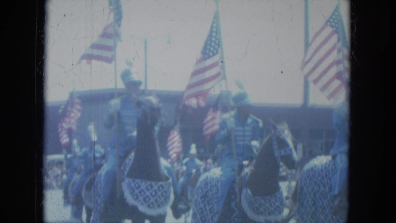 Mounted riders in blue uniforms carry American flags during a street parade.