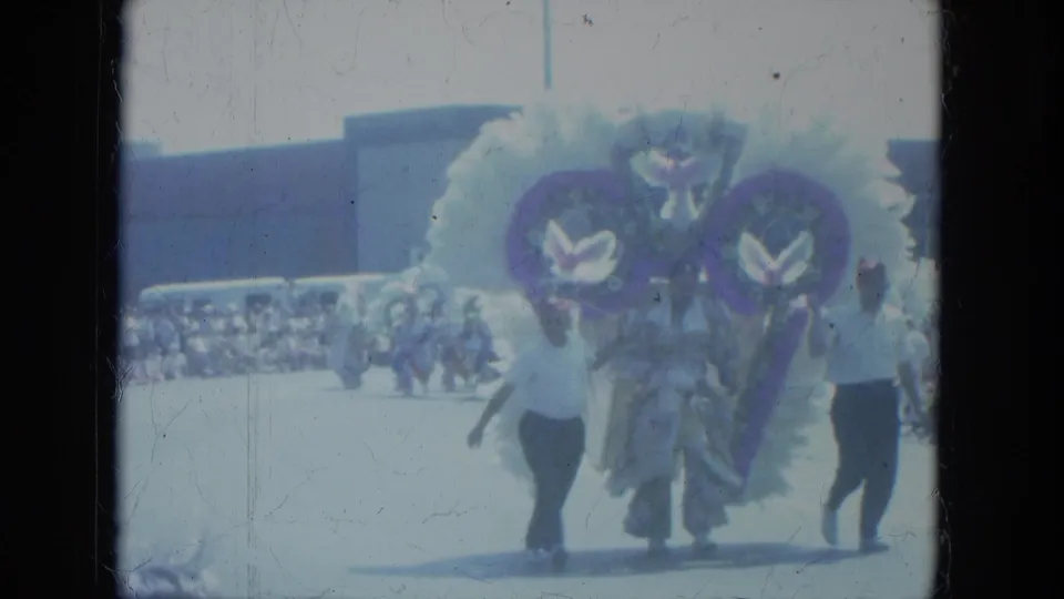 1966 Milwaukee parade frame with performers in large feathered white and purple costumes moving toward the camera.