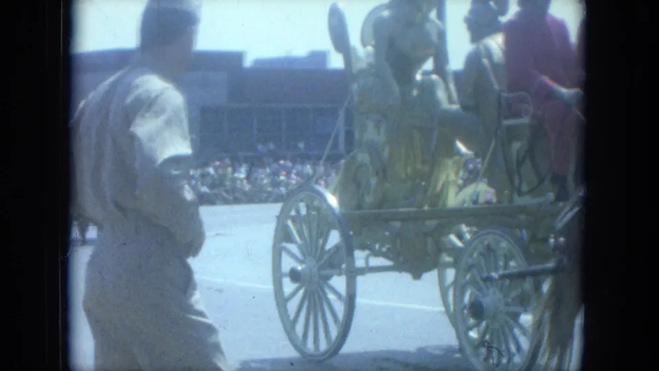 Costumed performers ride a horse-drawn circus float through a Milwaukee street as spectators watch in 1966 footage.