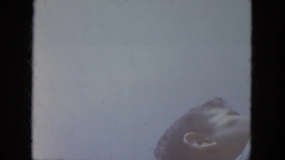 Brief 1966 Milwaukee home-movie frame showing a spectator's head at the lower right against a pale, overexposed background.