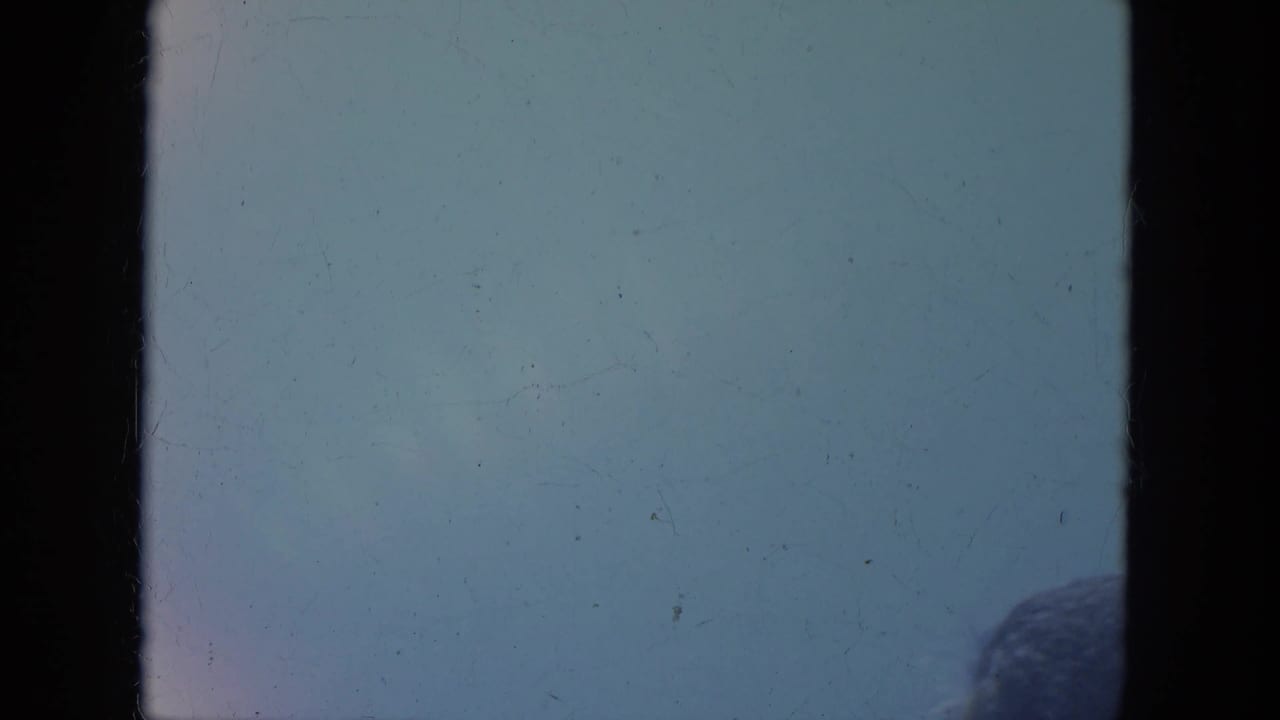 Washed-out 8mm frame from the Milwaukee parade clip, with a partial spectator head at the right edge.