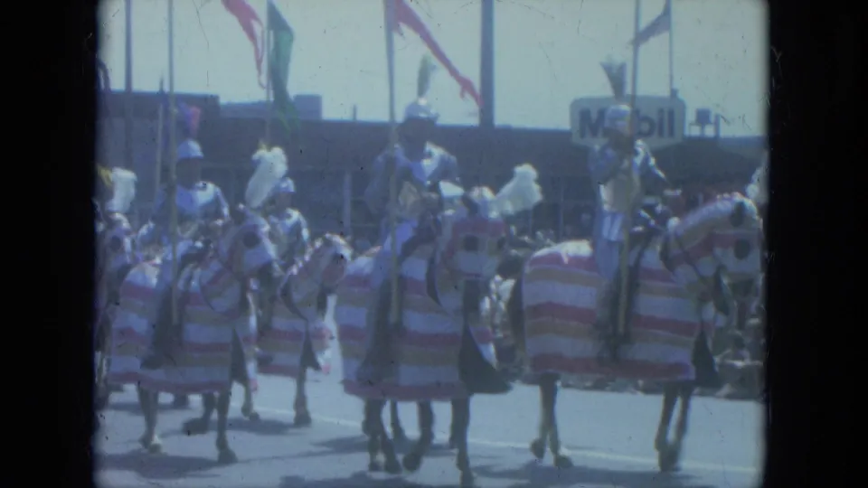 1966 Milwaukee parade view with costumed riders on decorated horses, striped blankets, flags, and a Mobil sign in the background.