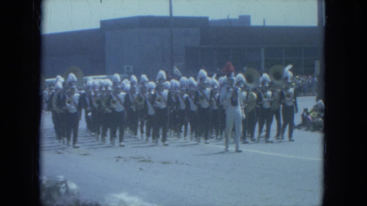 1966 Milwaukee parade view of a uniformed band playing in formation in front of a large public-looking building.
