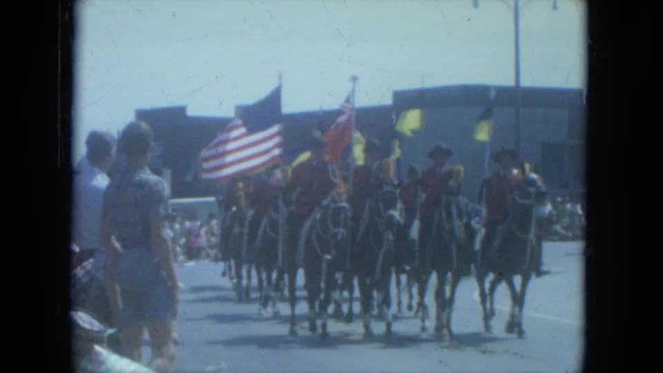 1966 Milwaukee parade frame showing riders on horseback carrying American and other flags past curbside spectators.