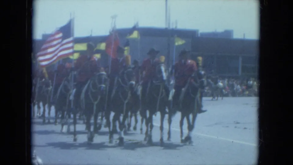 1966 Milwaukee parade view of riders on horseback carrying flags, including a large American flag, through a sunlit street.