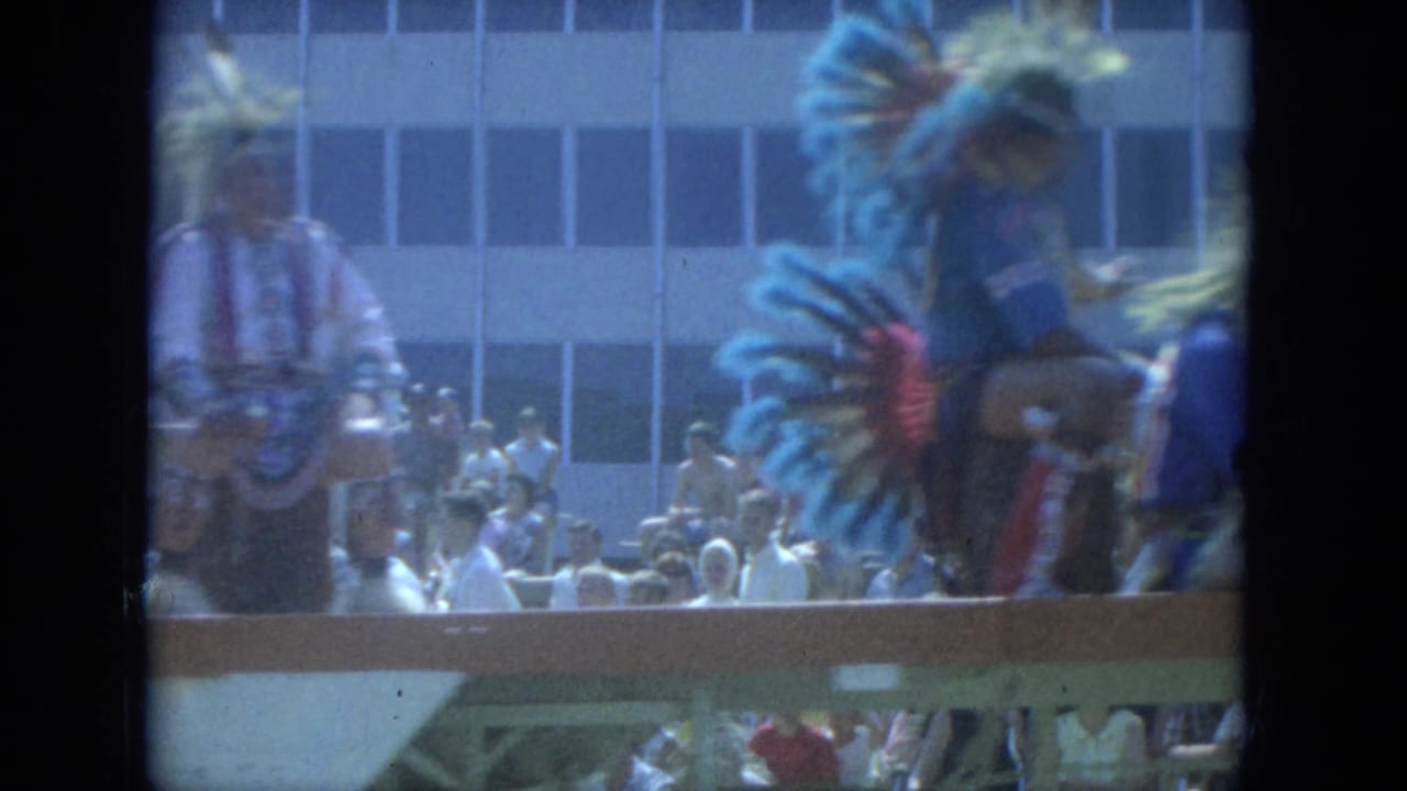 1966 Milwaukee parade view with a Native American participant in feathered regalia near a float and crowd.