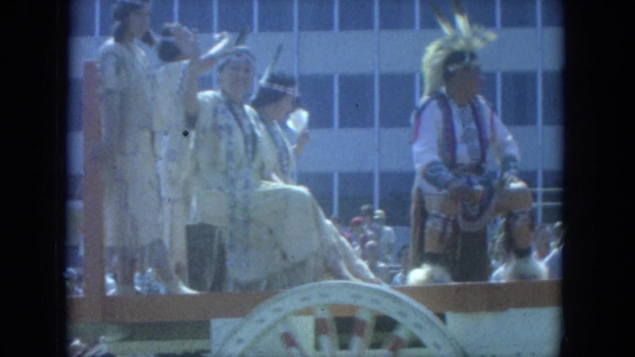 1966 Milwaukee parade float with people in ceremonial attire and a nearby Native American participant in feathered regalia.
