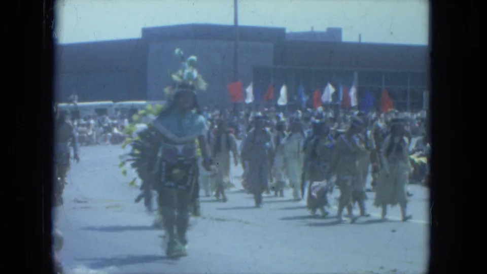1966 Milwaukee street parade with Native American participants marching in regalia before a crowd and flags.