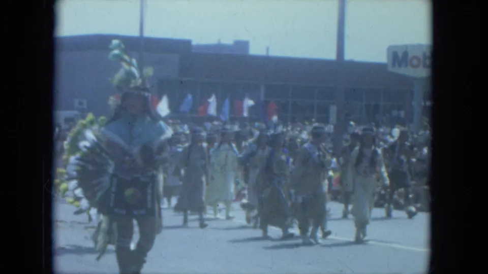 1966 Milwaukee parade participants in Native American regalia walk along the street near a visible Mobil sign.