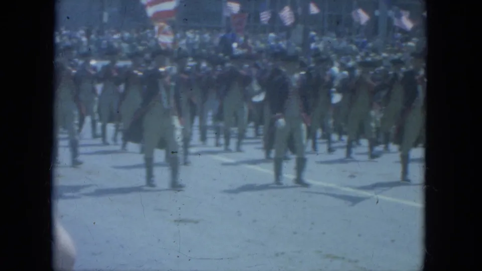 Men in colonial-style parade uniforms continue marching in formation on a Milwaukee street in 1966 home-movie footage.