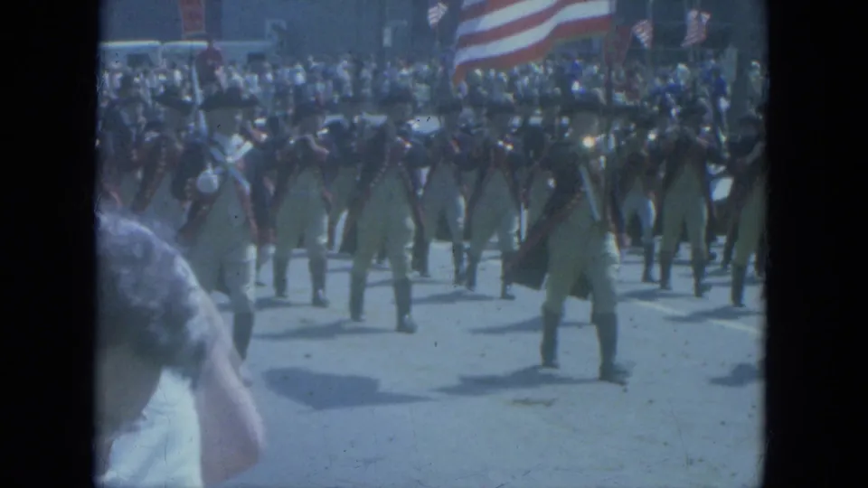 A closer 1966 Milwaukee parade frame shows Revolutionary War-style marchers with muskets and a large American flag overhead.
