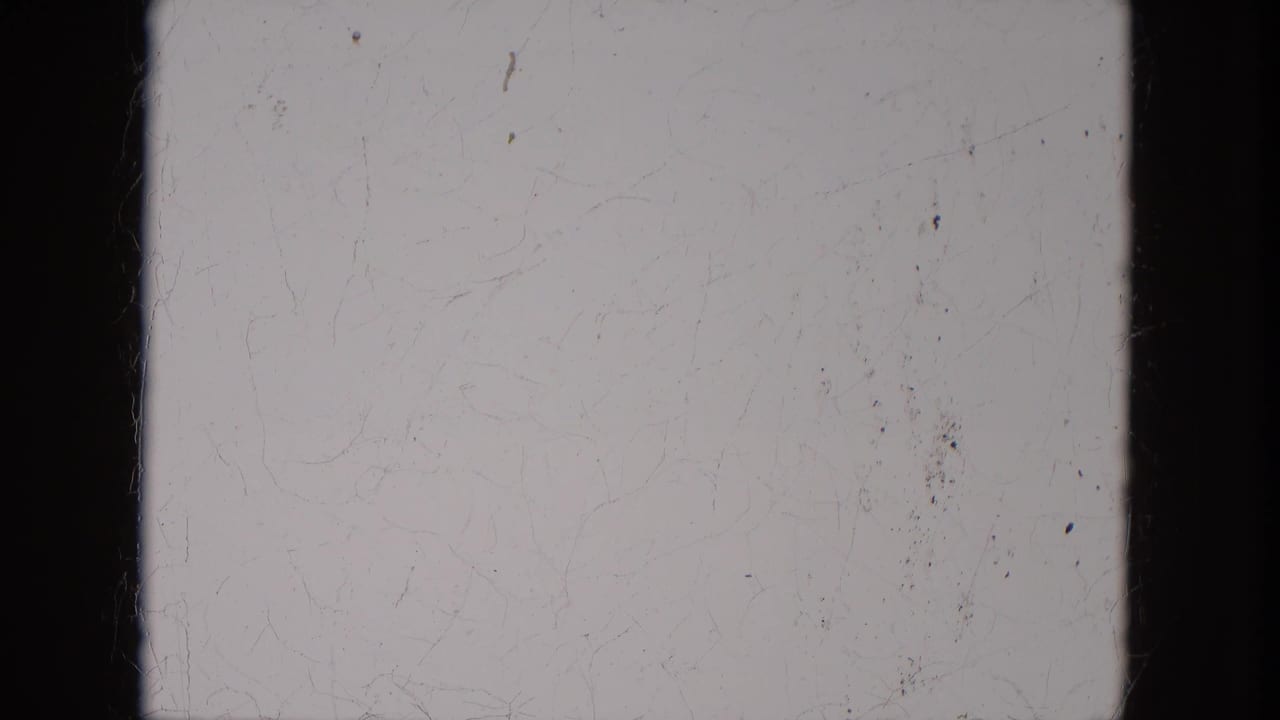 Blank or overexposed 8mm leader-like frame with black film edges, scratches, and dust visible.