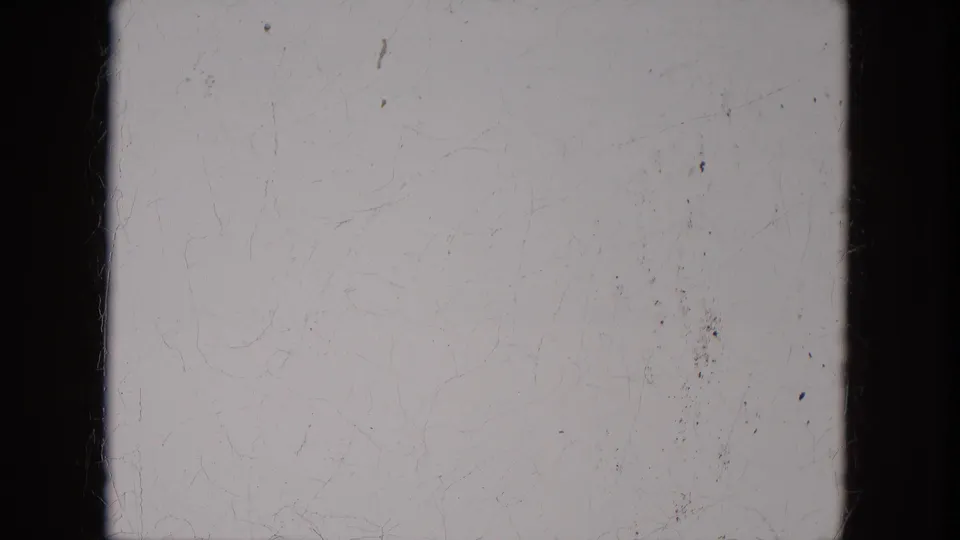 Blank or overexposed 8mm leader-like frame with black film edges, scratches, and dust visible.