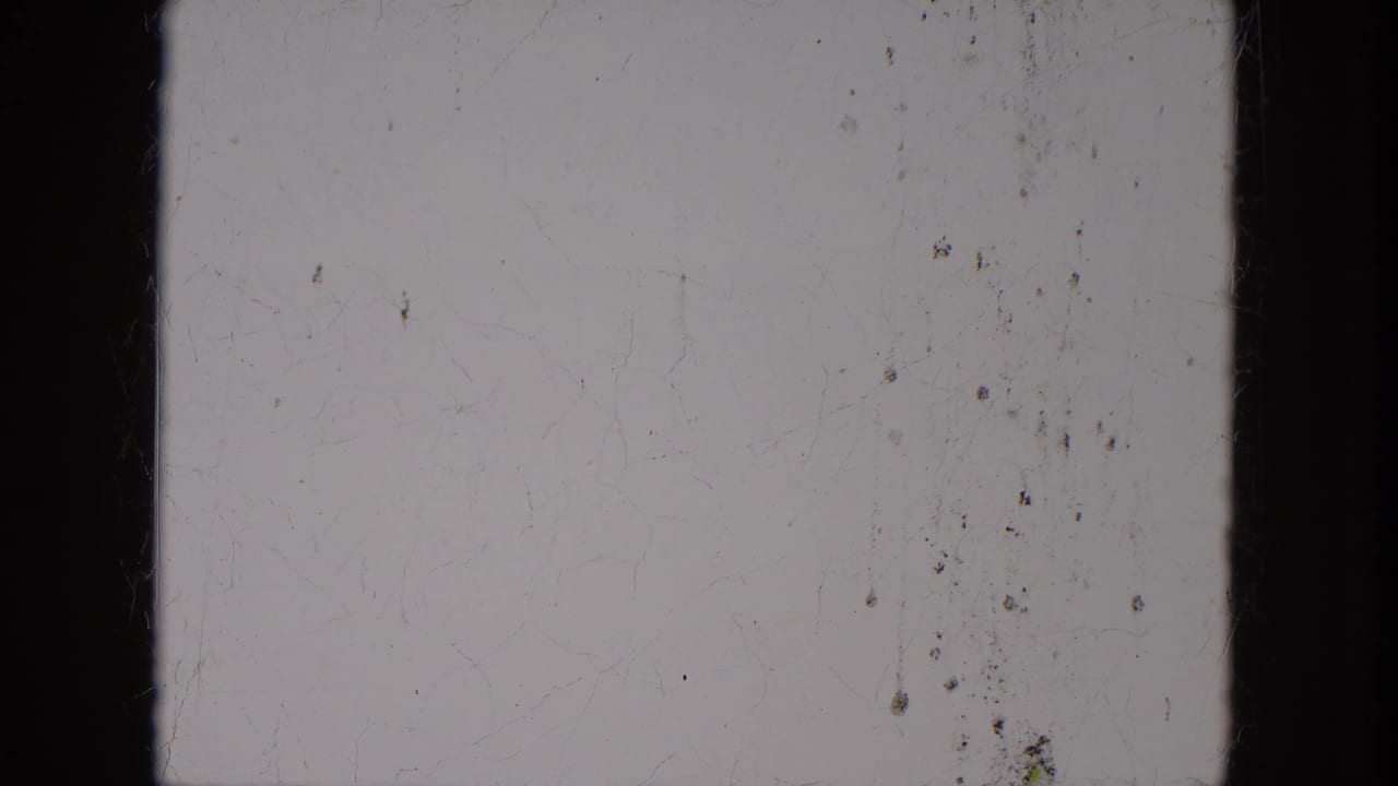 Overexposed or leader-like 8mm frame with pale center, dark vertical edges, dust, and light surface scratches.