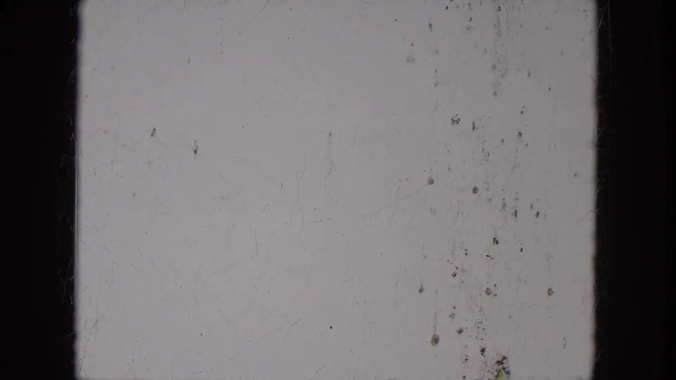 Overexposed or leader-like 8mm frame with pale center, dark vertical edges, dust, and light surface scratches.