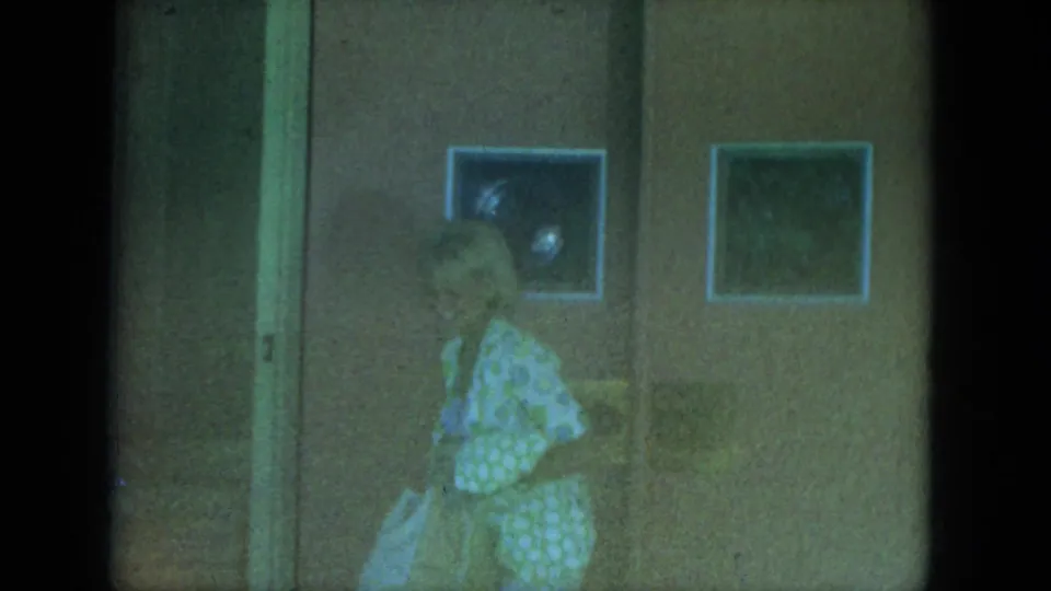 A woman in a light polka-dot dress carries a bag while walking past two framed pictures in a Milwaukee interior.