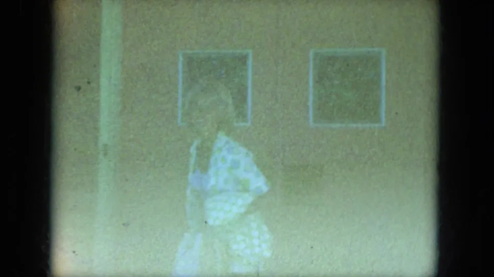The final frame shows the woman moving indoors under framed wall pictures, softened by grain and pale green-yellow exposure.