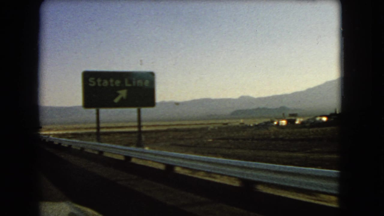 Roadside State Line sign beside a desert highway and guardrail.