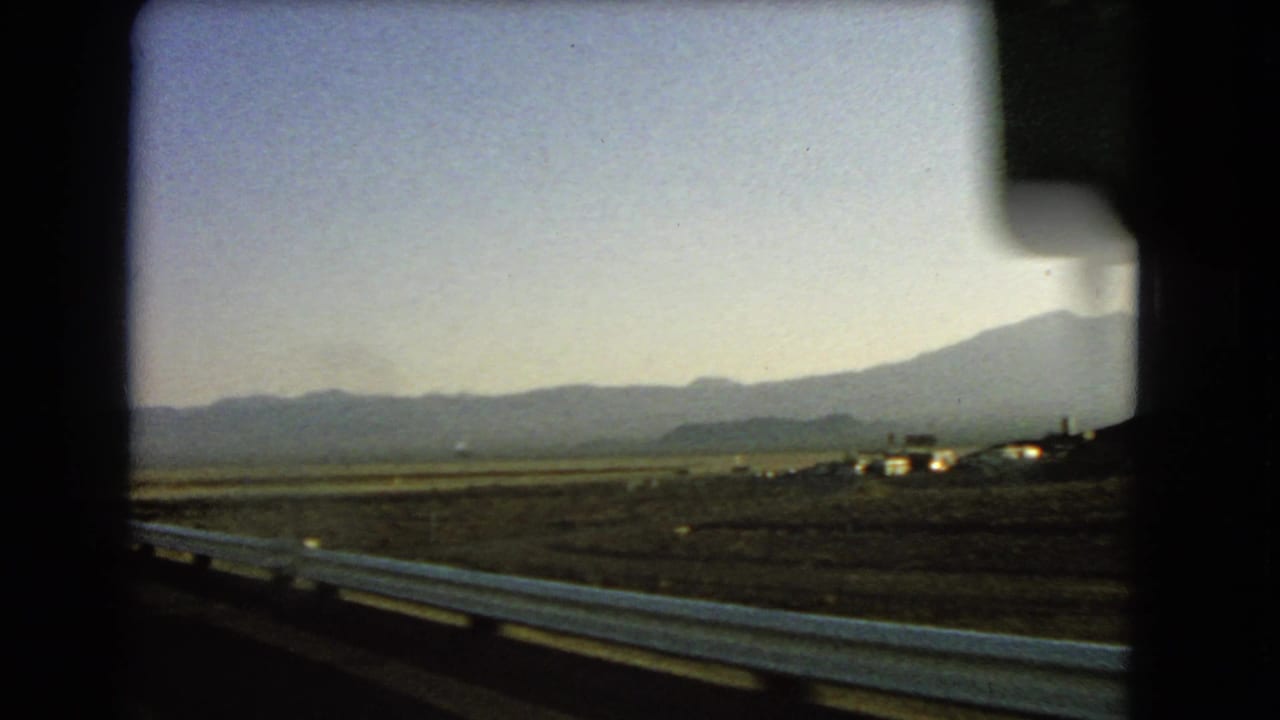 Desert highway view with guardrail and mountains in the distance.