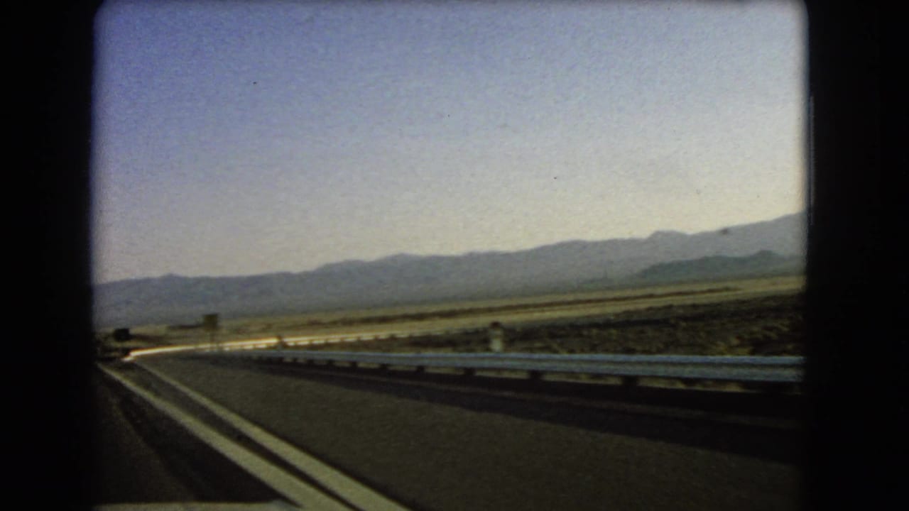 Paved desert highway curving beside a metal guardrail with mountains in the distance.