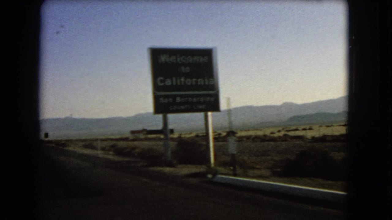 Moving car view passing a Welcome to California sign beside a desert highway.