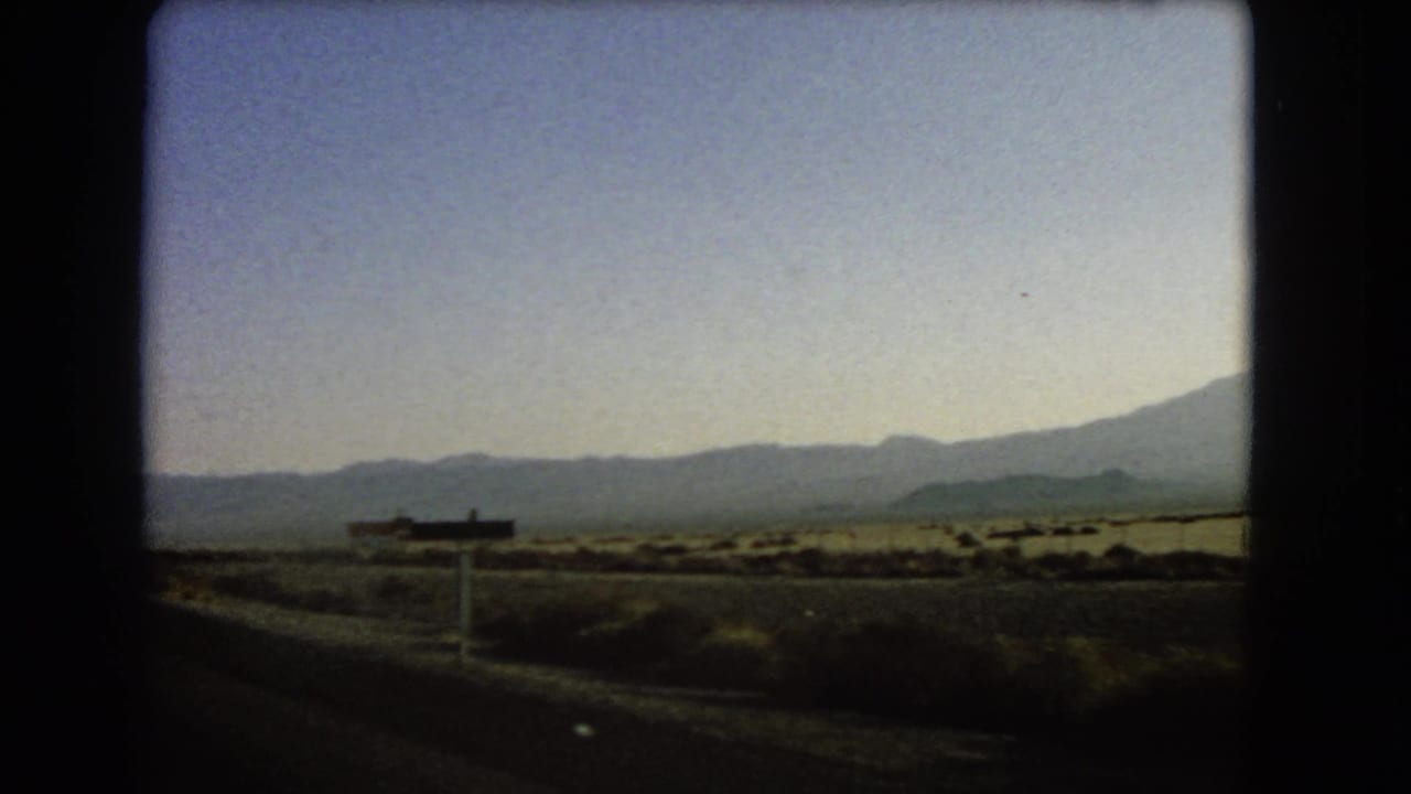Desert roadside and distant mountains seen from a moving vehicle after passing the sign.