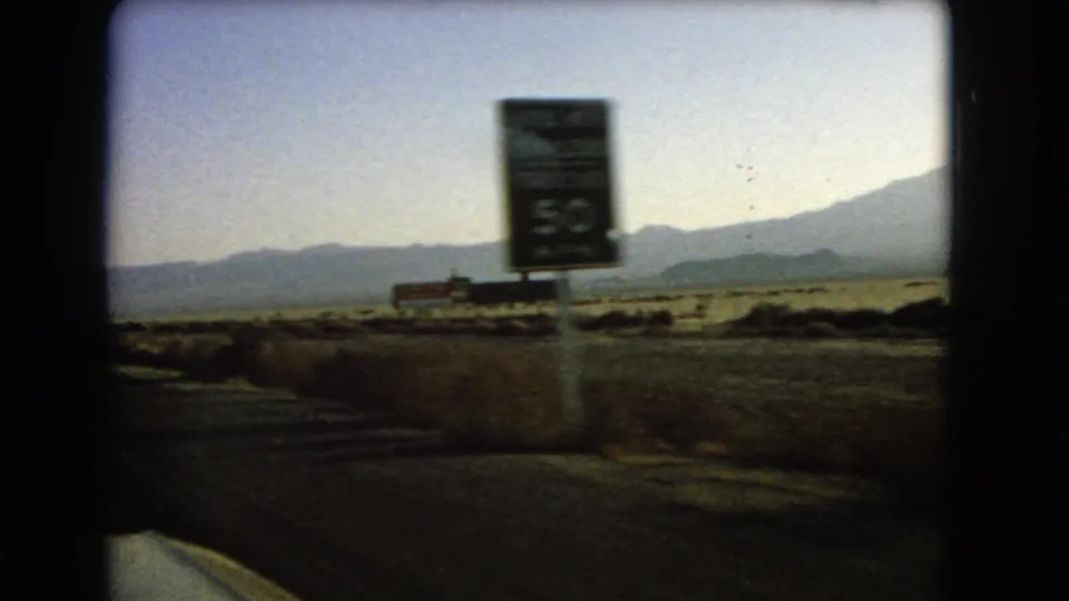 1966 Nevada road-trip footage showing desert scrub, distant mountains, and a blurred roadside sign viewed from inside a moving car.