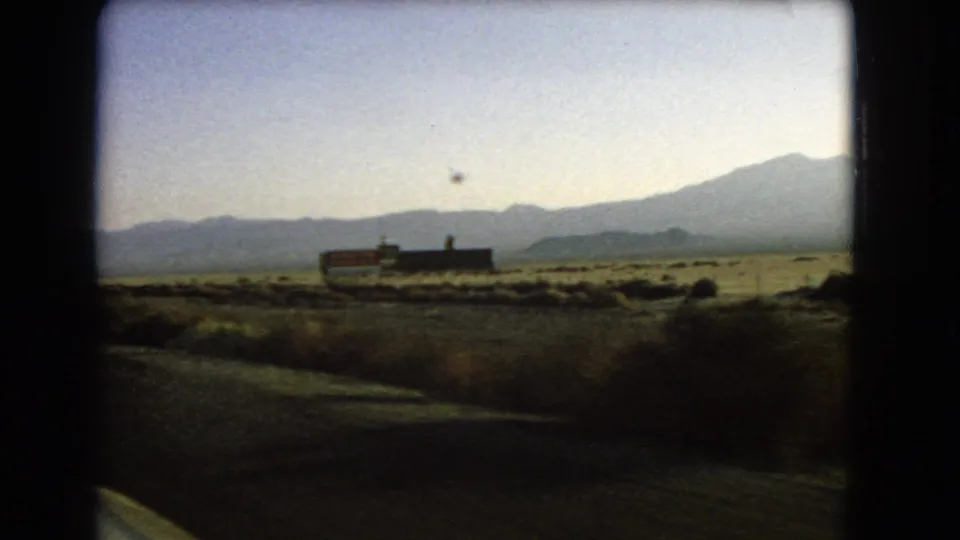 1966 Nevada desert highway view with low roadside signage, dry scrub, and a mountain range beyond the road shoulder.