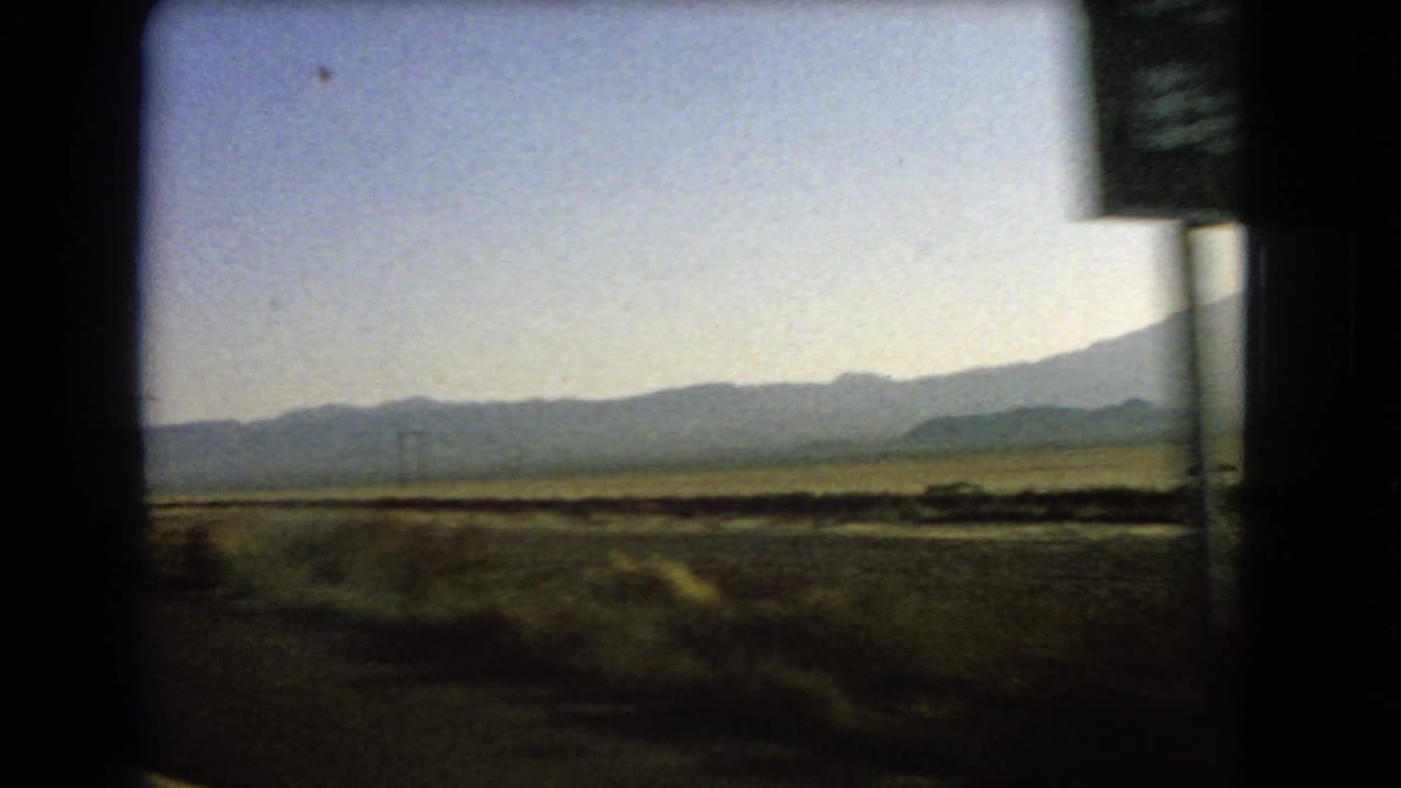A moving-car view across Nevada desert scrub toward distant mountains, with a roadside sign partly cropped at the right edge.