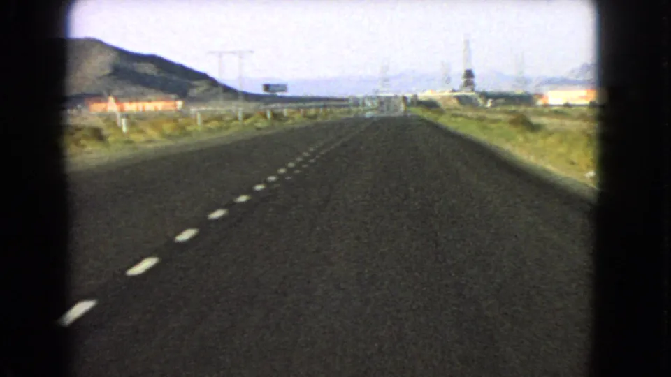 The Nevada highway view shows dashed lane markings, a roadside sign, power lines and desert mountains under a bright sky.