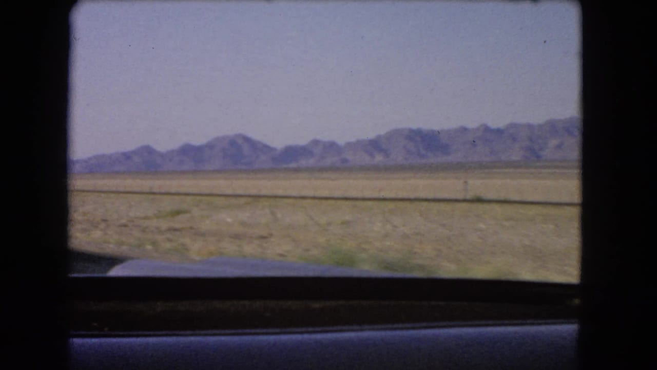 Desert plain and distant mountains seen through a vehicle window.