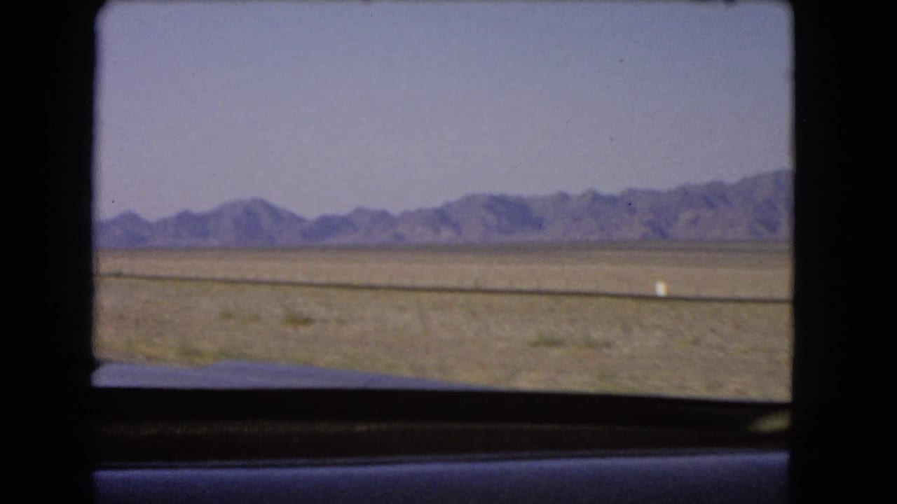 1966 Nevada desert landscape with distant mountains, viewed through a dark-framed car window on 8mm film.