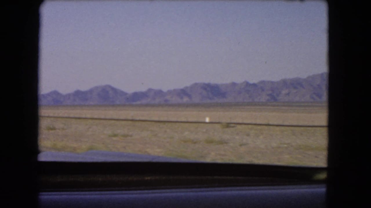 Mountain horizon across a dry plain viewed from inside a car.