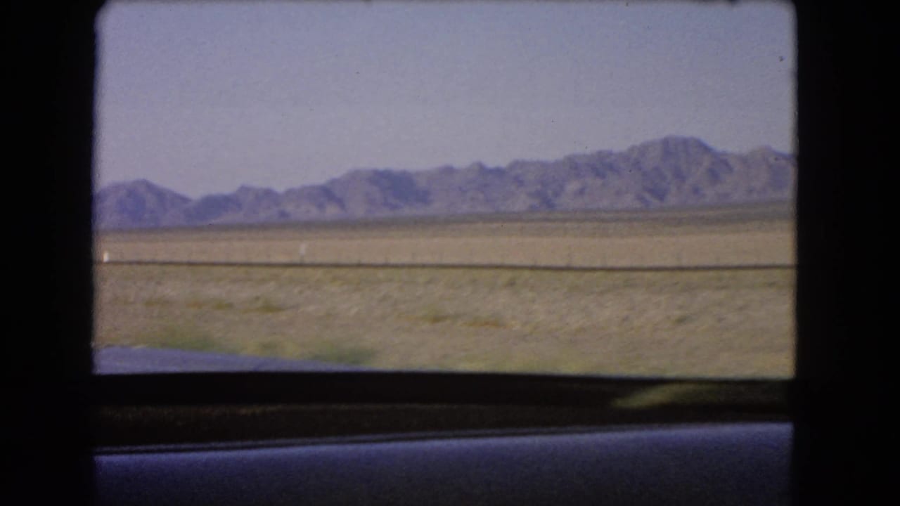 Distant mountains and desert plain seen through a moving vehicle window.