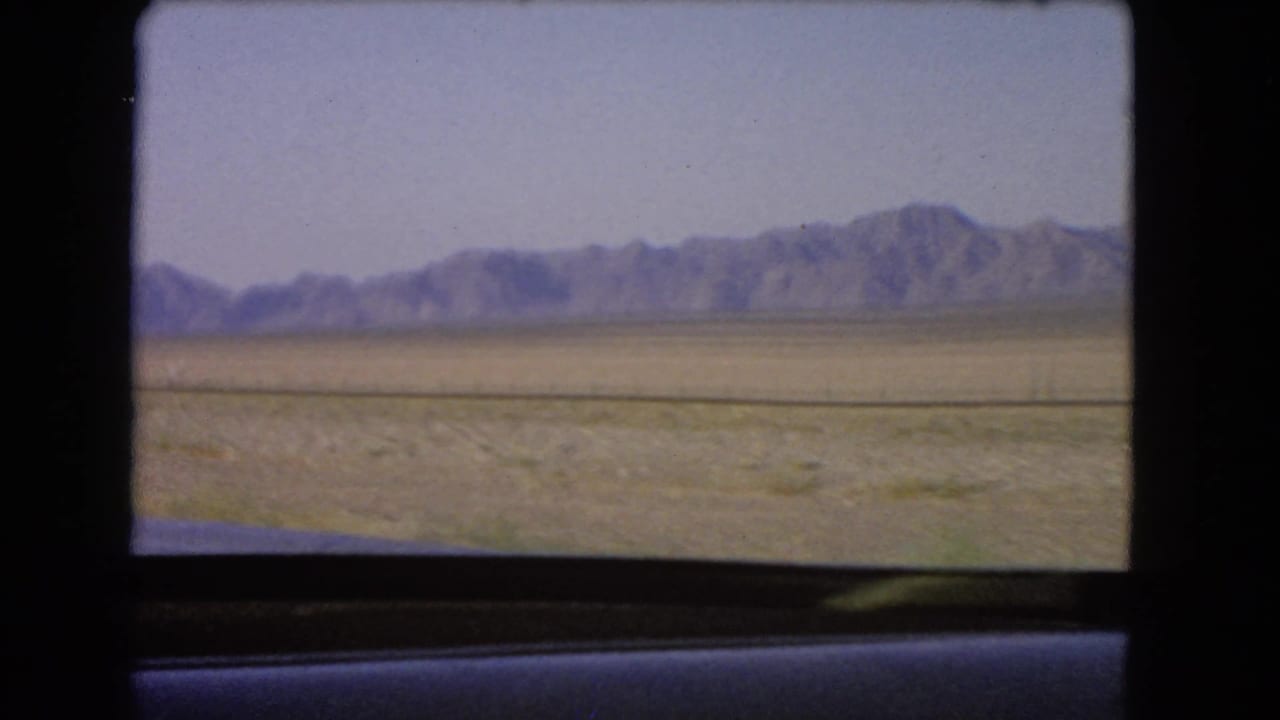 Flat desert and mountain range passing outside a vehicle window.