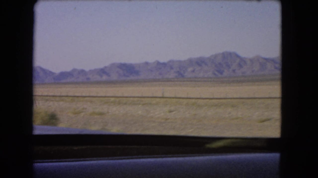 1966 home-movie frame of dry Nevada terrain and distant mountains, filmed from a moving vehicle window.