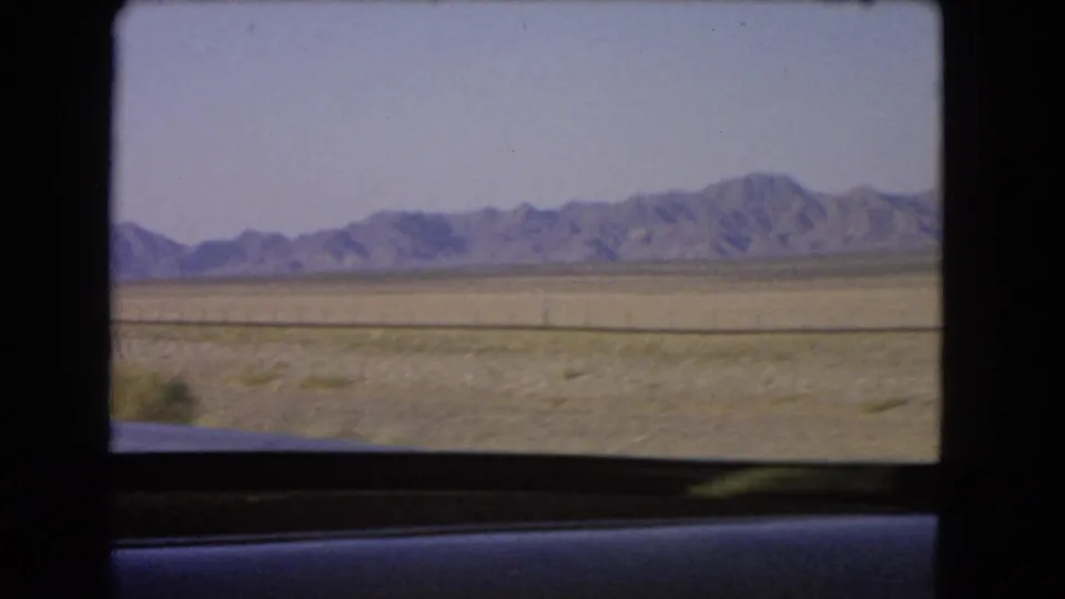 1966 home-movie frame of dry Nevada terrain and distant mountains, filmed from a moving vehicle window.