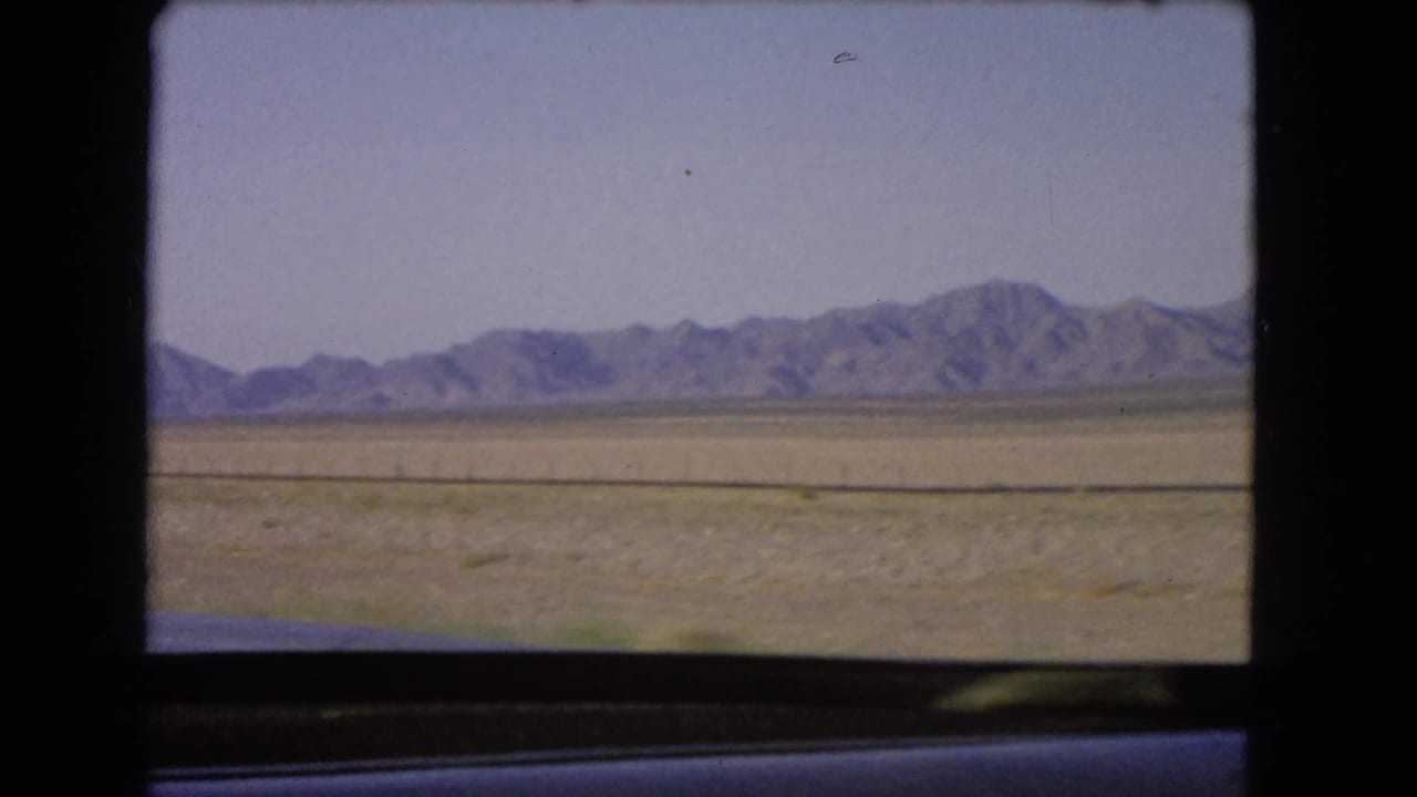 Arid Nevada plain and distant low mountains seen through a vehicle window in 1966 8mm footage.