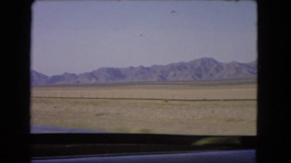 Arid Nevada plain and distant low mountains seen through a vehicle window in 1966 8mm footage.