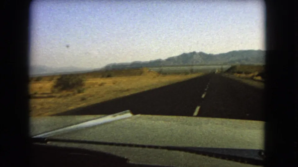 1966 Nevada 8mm view from inside a moving car on a straight desert highway toward distant mountains.