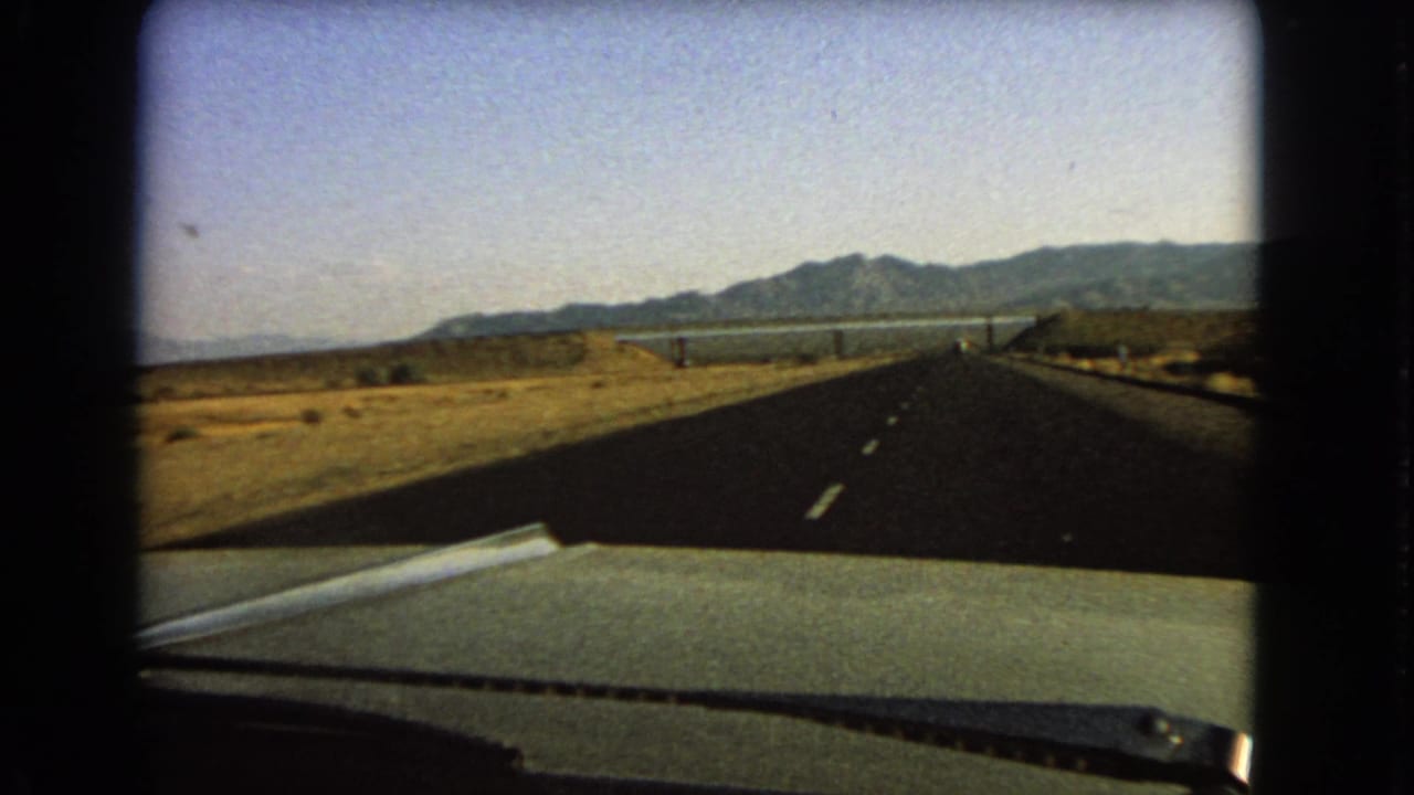 1966 Nevada road view from a car, with the highway running toward mountains and a broad reservoir-like water body.