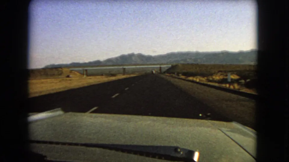 Final 1966 Nevada frame from inside a car, showing a straight desert highway leading toward distant water and mountains.